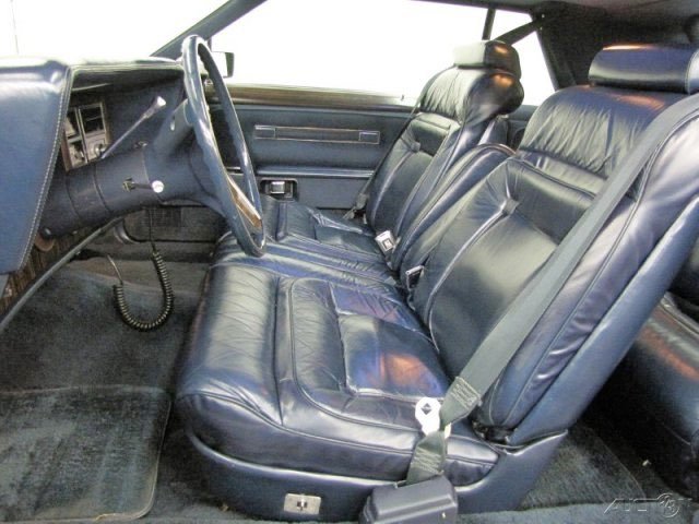 The interior of a vintage car featuring dark blue leather seats, steering wheel, dashboard, and seat belts.