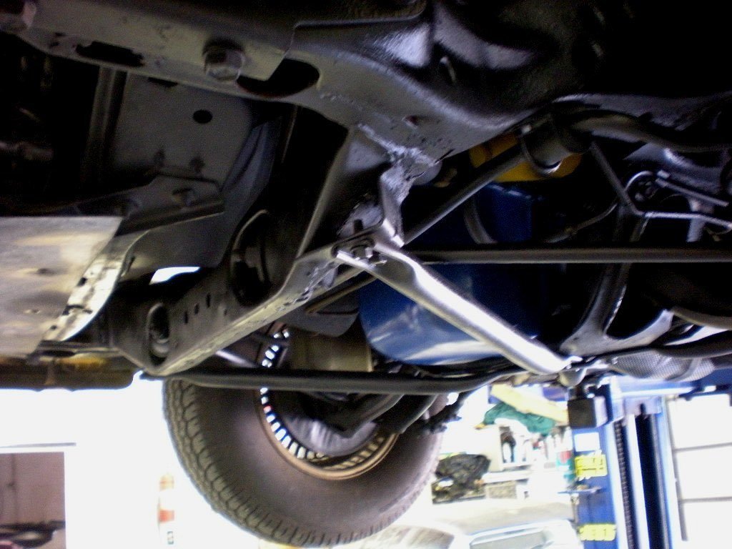 Underneath view of a vehicle showing the chassis and suspension components, with a tire visible in the background.