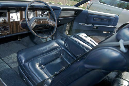 Interior of a vintage car with blue leather seats, wooden dashboard, and steering wheel.