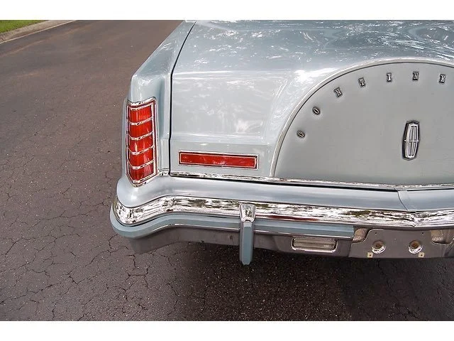 Close-up of the rear end of a vintage light gray Oldsmobile car, showing taillights, chrome bumper, and the Oldsmobile emblem on the trunk.