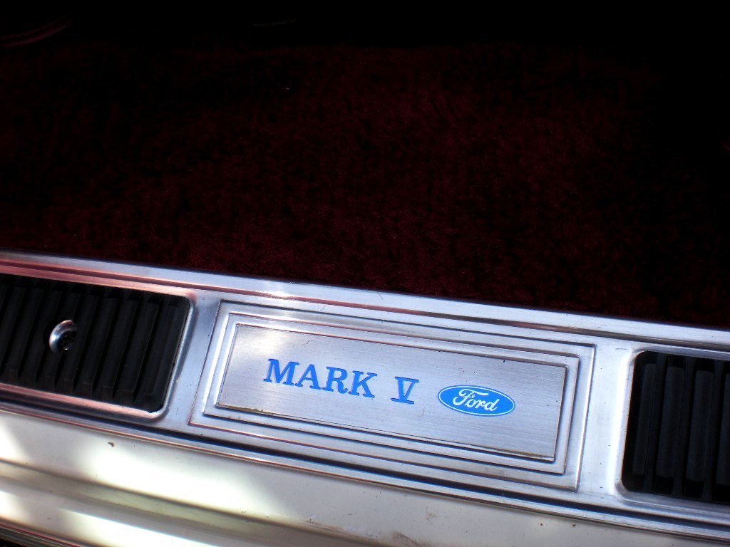 Close-up of a car's front grille and bumper with a dealership emblem that reads 'MARK V' with a Ford logo