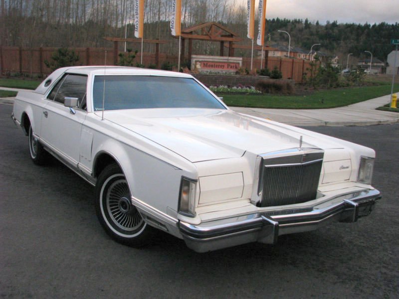White vintage luxury car parked on the street with Monastery Park sign and trees in the background.