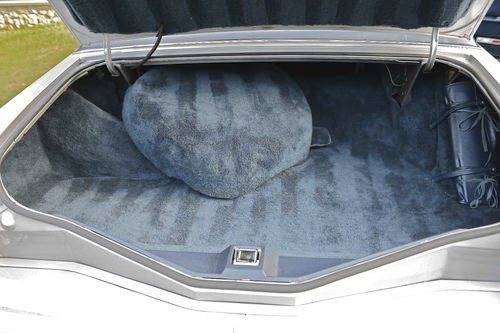 The open trunk of a car with a gray carpeted interior and a circular gray carpet piece inside.