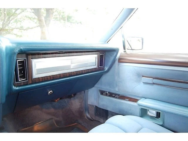 Interior of a vintage car dashboard featuring a large horizontal radio and blue upholstery.