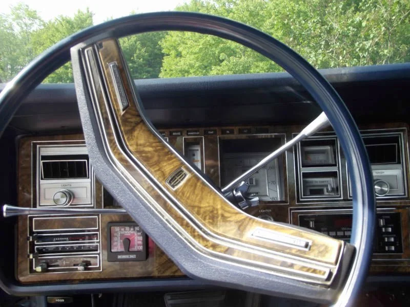 Close-up of a vintage car dashboard with wood paneling, featuring a steering wheel, gauges, and controls.