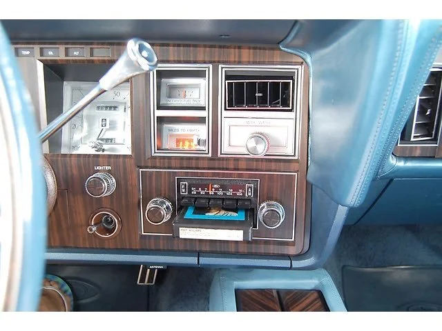 Dashboard of a vintage car featuring a radio, climate control, switch panel, and wood grain accents.