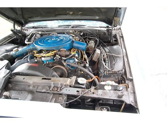 Inside view of a car engine bay showing a blue engine air cleaner, various hoses, wires, and components.