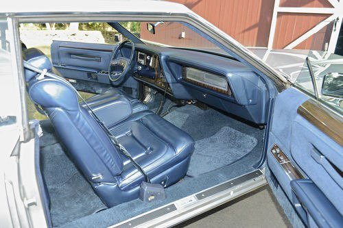 Interior of a vintage car with blue leather seats, dashboard, and steering wheel.