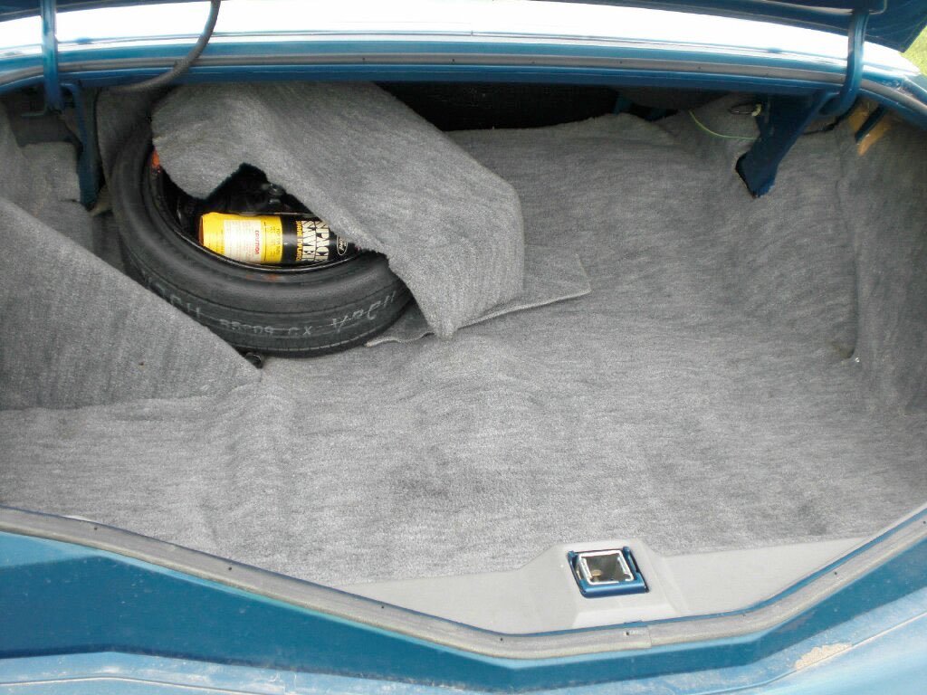 Rear trunk of a car with a spare tire, a bottle of oil, and a gray fabric cover inside.