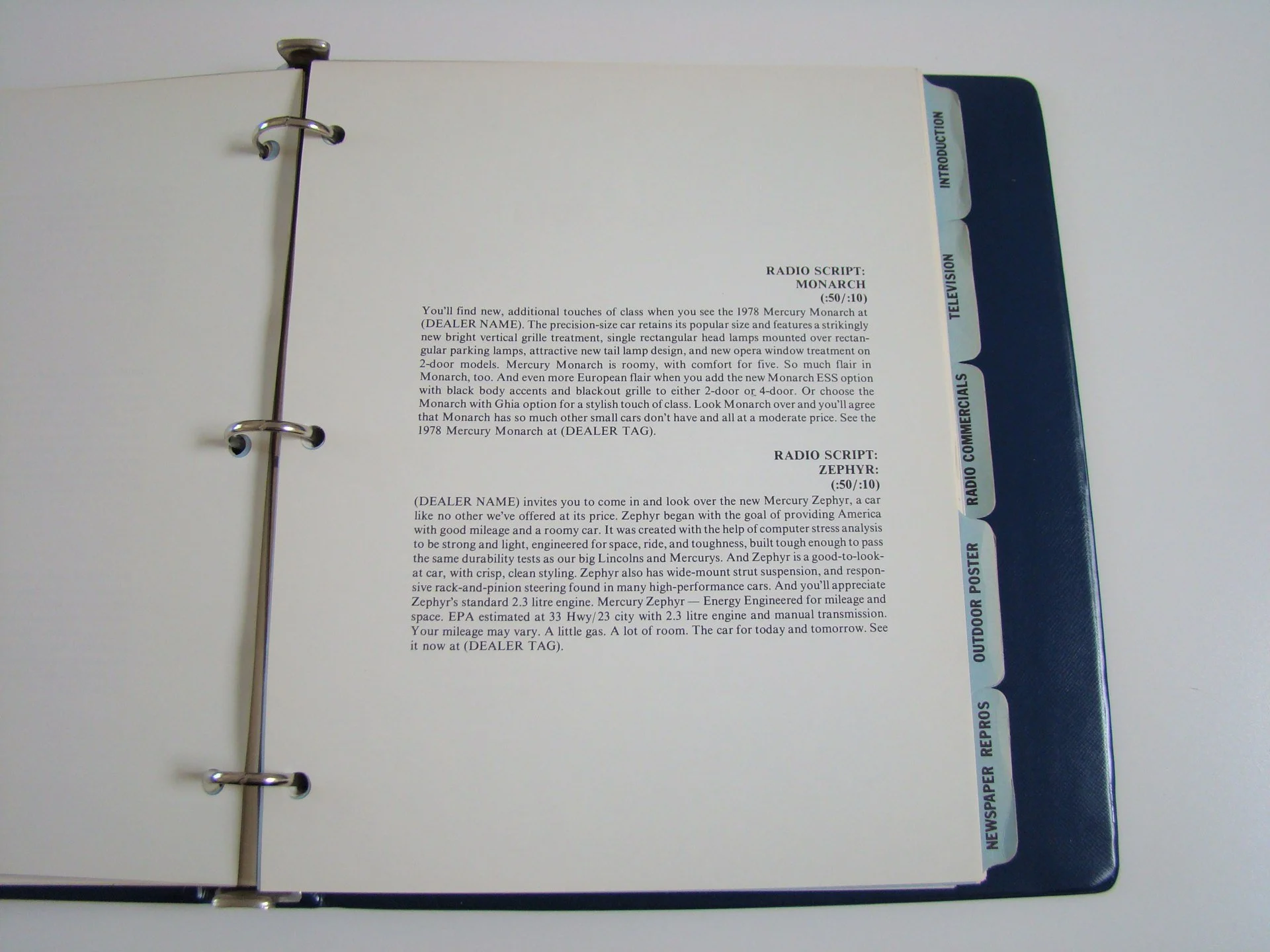 Open binder with typed car advertisement page andblue tabbed section on the right labeled with categories for radio scripts, television, commercials, radio, outdoor poster, newspaper repros.