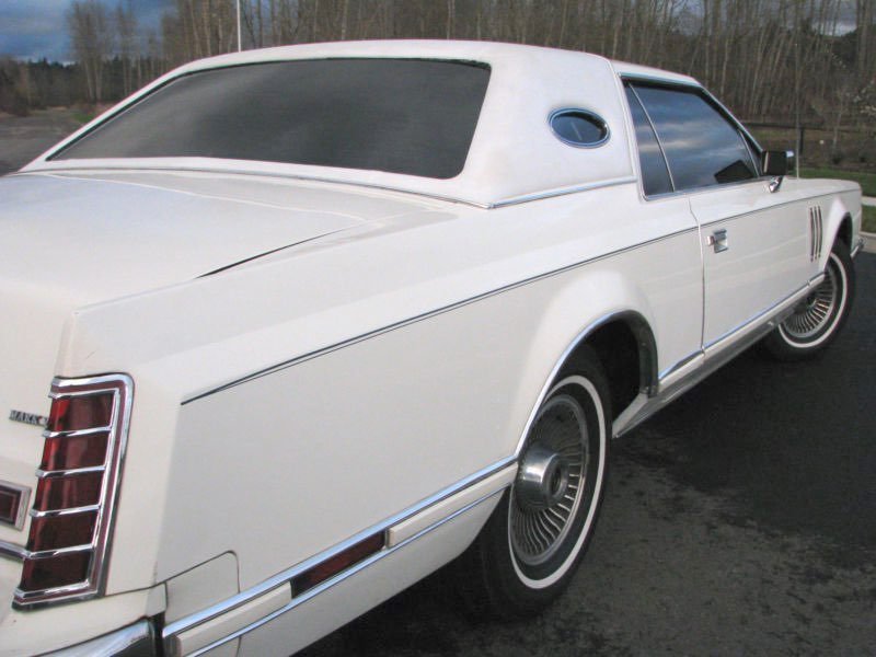 A vintage white luxury car parked outdoors on a paved surface, with a sleek design, tinted windows, and wire-spoke hubcaps.