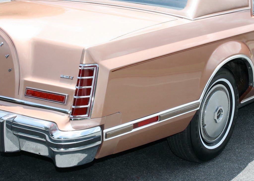 Close-up of the rear side of a vintage pink Lincoln Mark V car, showing tail light, chrome bumper, and part of the rear wheel.