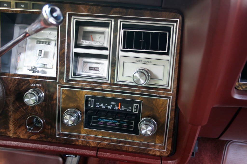 Close-up of a vintage car dashboard with wood grain finish, including an analog radio, gauges, and switches.