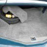 Close-up of a gray carpeted car floor with a small piece of yellow trash and a black car mat.