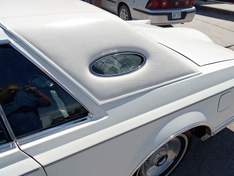Close-up of the roof of a white vintage car with an oval-shaped glass window.