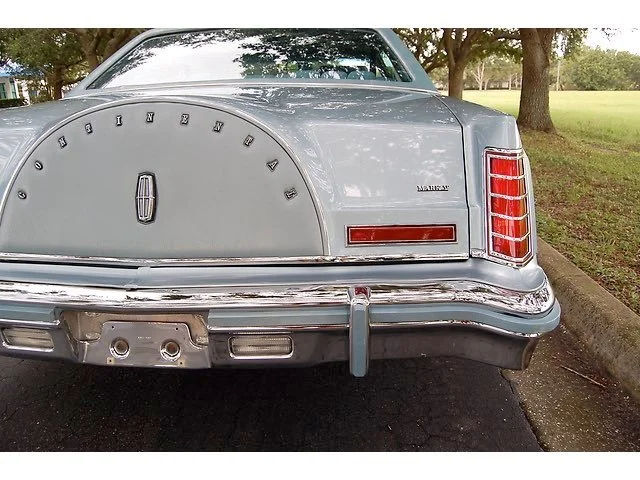 Rear view of a vintage silver Mercury Marquis car parked on a street with trees in the background.