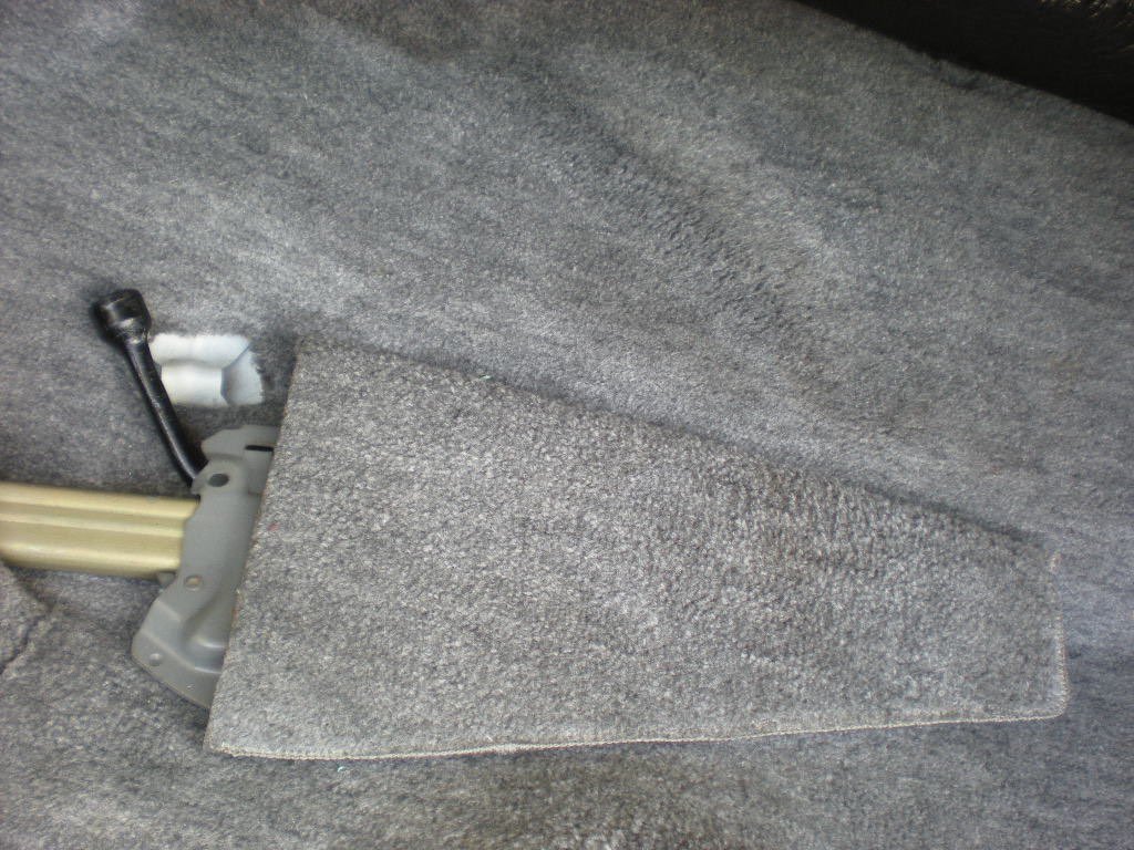 Close-up of a gray automotive carpeted floor mat with a metal latch and a small black lever attached.