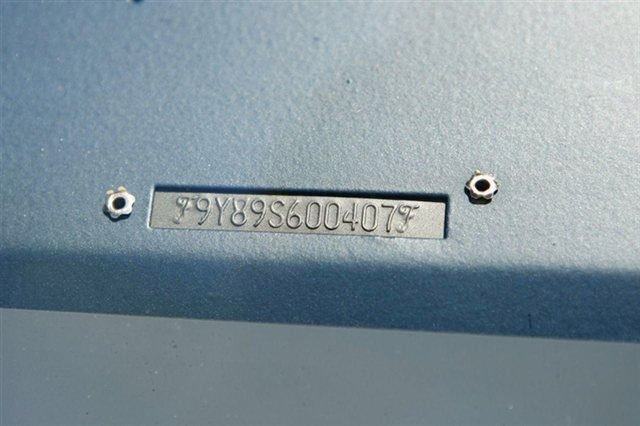 Close-up of a metal panel with a rectangular serial number plate and two screws.