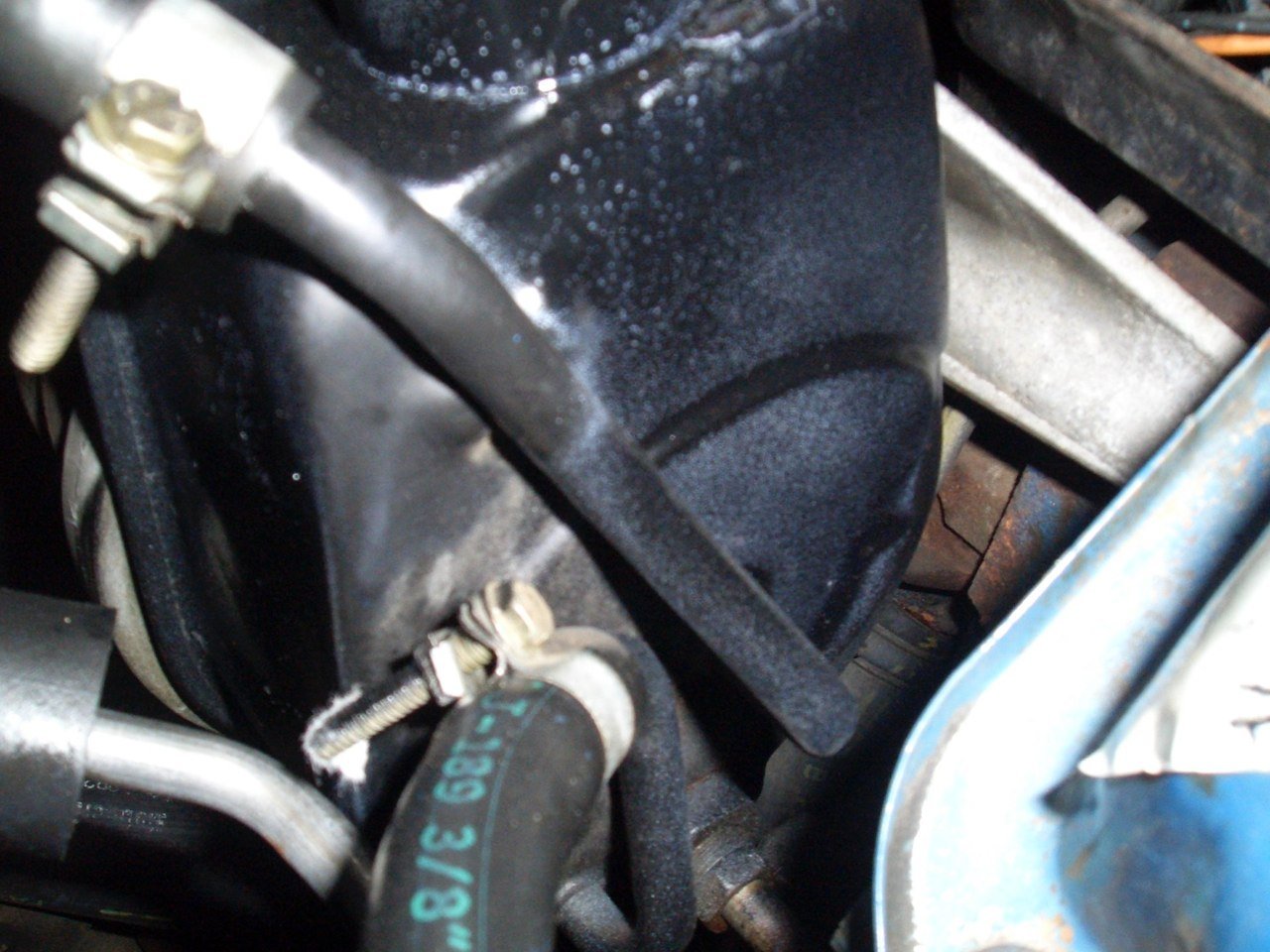 Close-up of a mechanical engine part with hoses, bolts, and metal components.