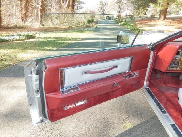 Open car door showing red and white interior panel with a handle, control panel, and silver accents.