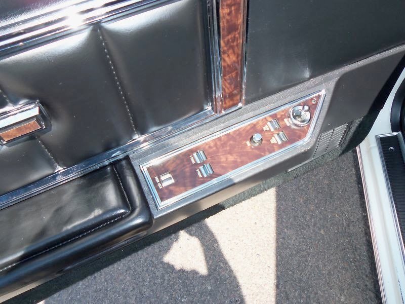Close-up of car interior showing woodgrain panel with control switches and knobs on the door.