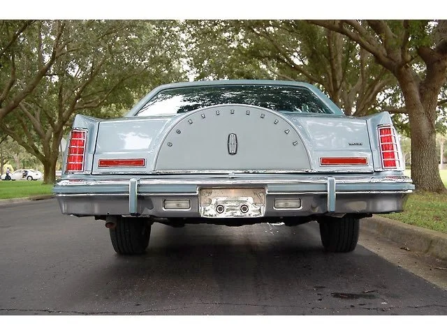 Rear view of a vintage light blue Lincoln Continental car parked on a street with trees on both sides.