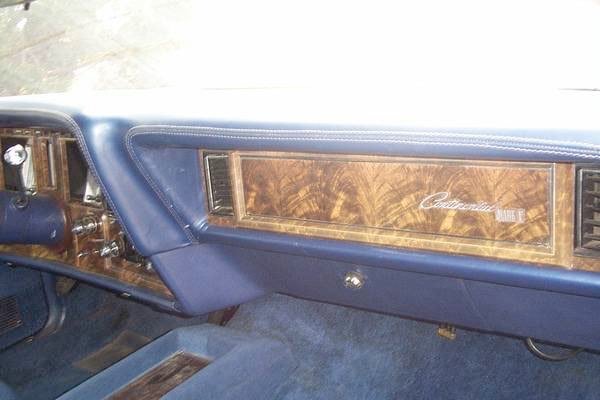 Close-up of the dashboard inside a vintage car, featuring woodgrain paneling and blue upholstery.