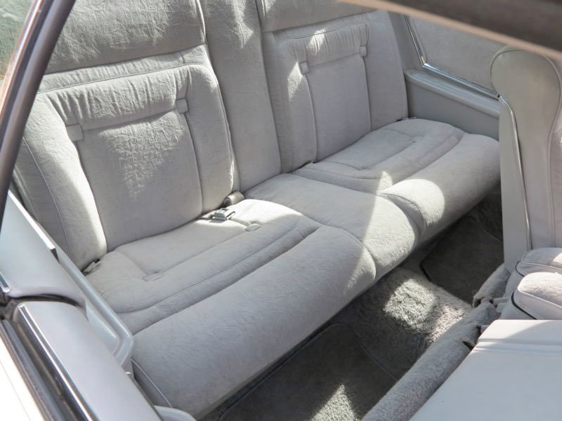 Interior of a vintage car showing beige fabric upholstered backseat and part of the side door panel.