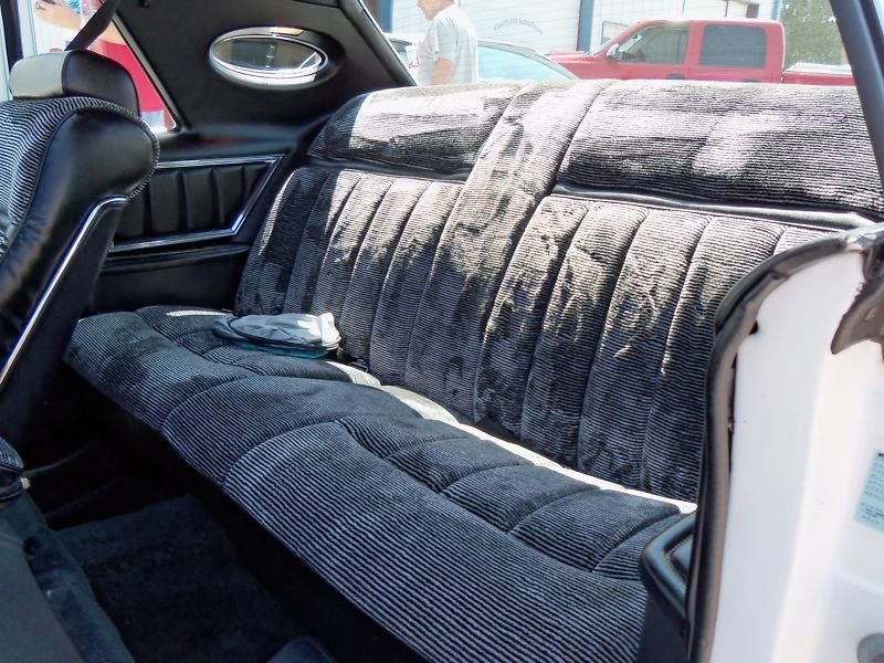 The backseat of a car with dark, plush velvet upholstery and quilted patterns, with a small white item placed on it.