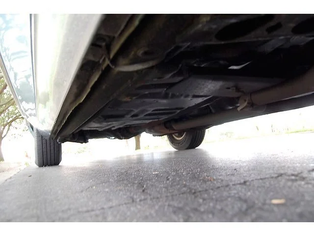 View of the underside of a vehicle showing parts of the exhaust system and suspension, with the ground visible below.