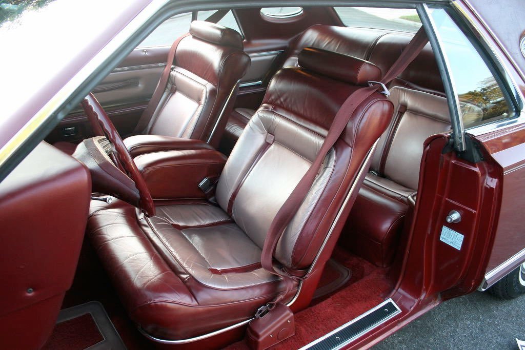 Interior of a vintage car with burgundy and tan leather seats, including a front bench seat, steering wheel, and a wood-trimmed dashboard.