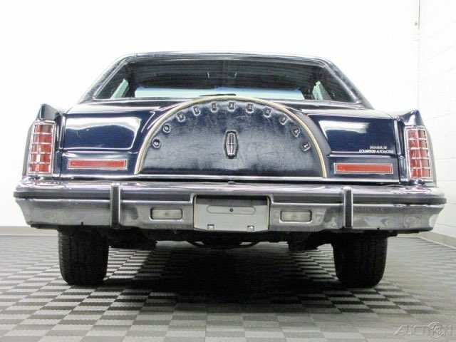 Rear view of a vintage black Lincoln Continental Mark VI car showing the spare tire cover on the trunk with the Lincoln emblem and the style of the tail lights and bumper.