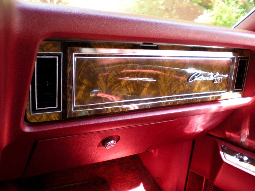 Close-up of a vintage car dashboard with a woodgrain panel, red interior, and a badge that reads 'Chrysler Newport'.