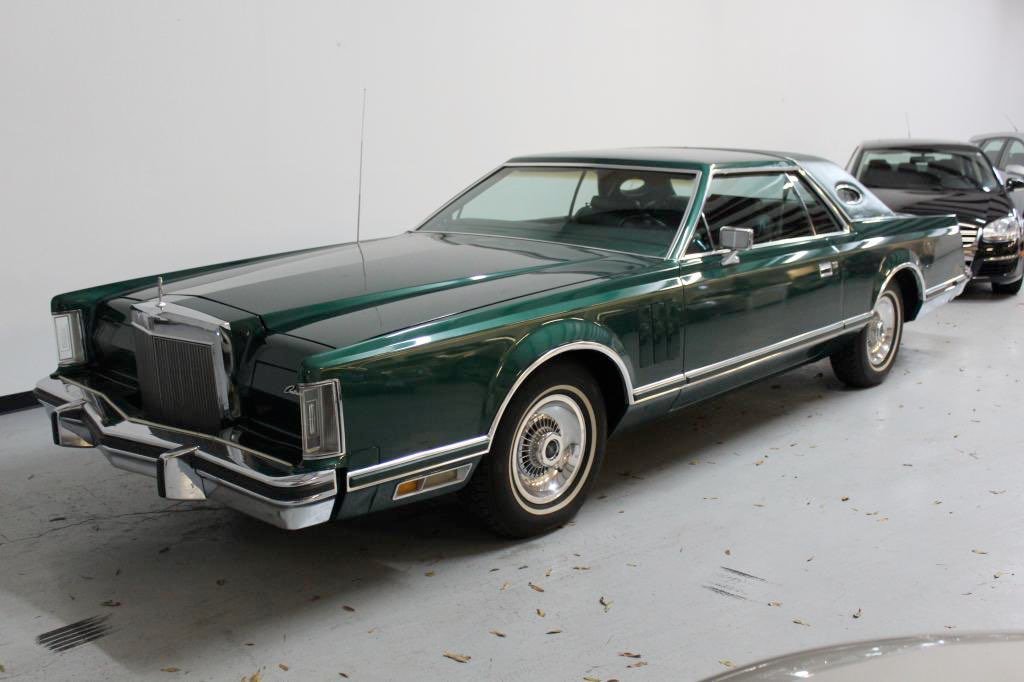 A vintage green classic car with a sleek design, parked indoors with other vehicles in the background.