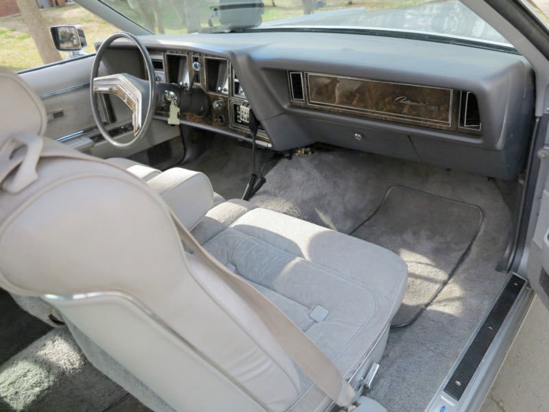 Interior view of a vintage car's front passenger area, showing the dashboard, steering wheel, and front seats with light-colored upholstery.