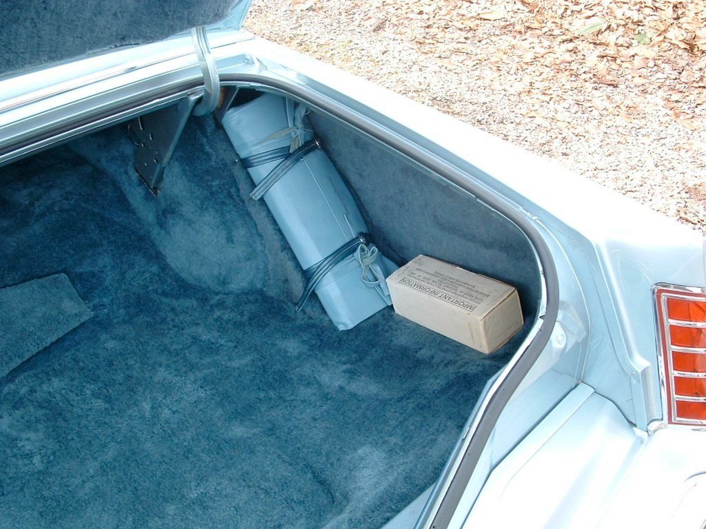 The trunk of a light blue vintage car with two wrapped packages and one small cardboard box inside