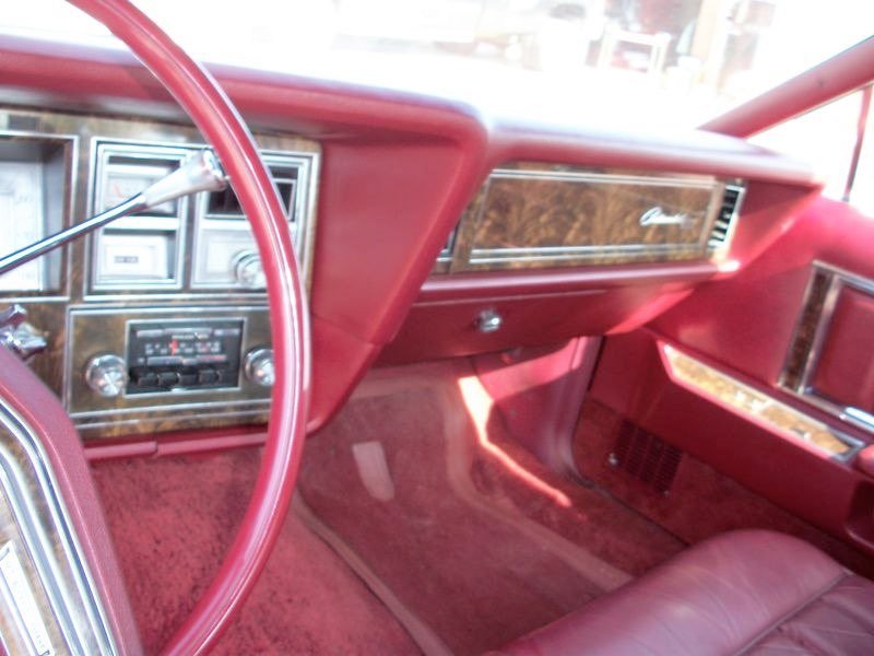 The interior of a vintage car, featuring red leather seats, a wood-paneled dashboard, and an old-fashioned radio and control panel.