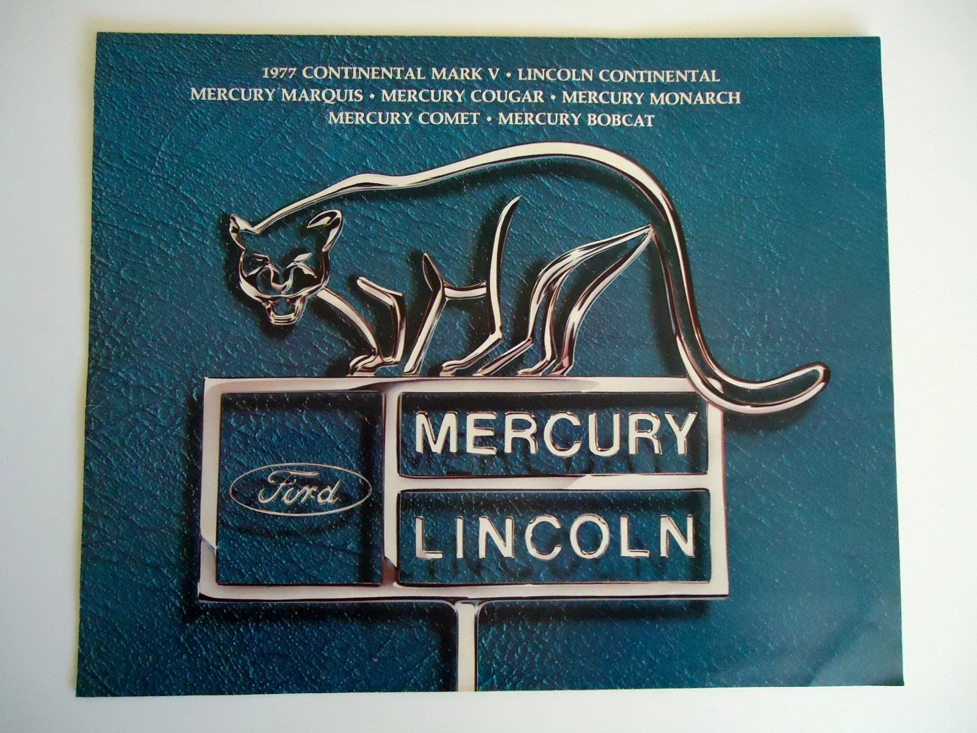 A vintage Mercury car emblem with a black panther figurine on top, and a backdrop referencing various Mercury car models from 1977, along with a Ford logo.