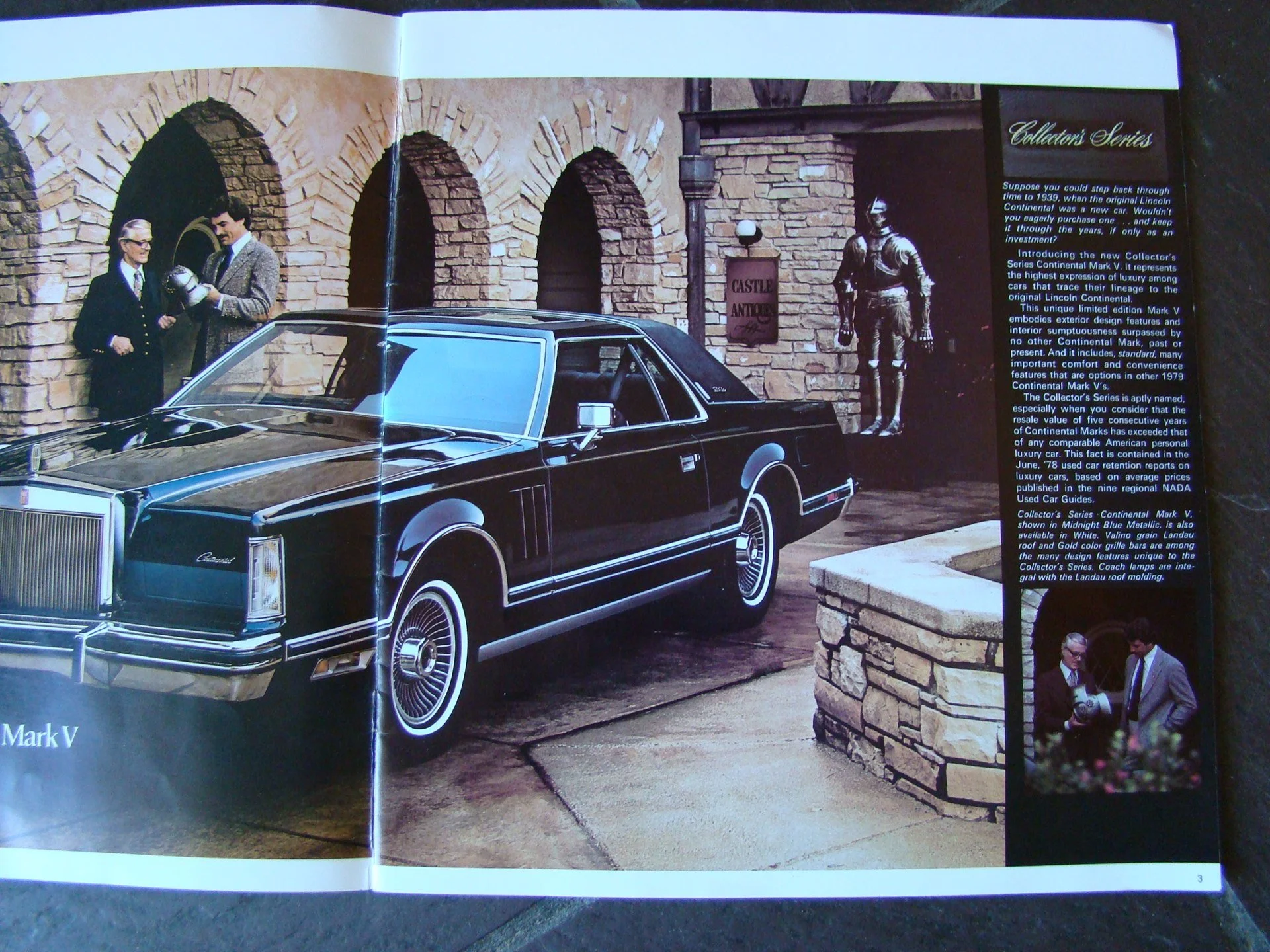 A vintage black Lincoln Continental Mark V car parked in front of a brick building with two men in suits inspecting it and a statue of a soldier in the background.