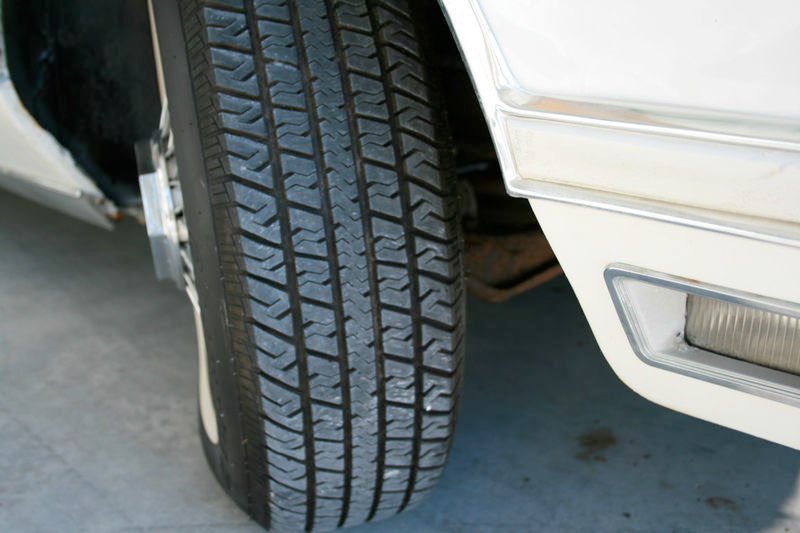 Close-up of a car tire and part of the front bumper on a white vehicle.