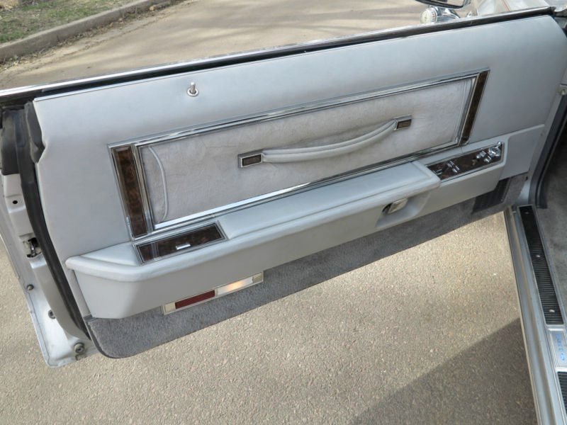 Close-up of a vintage car door interior with gray upholstery, a wooden trim, and control buttons.