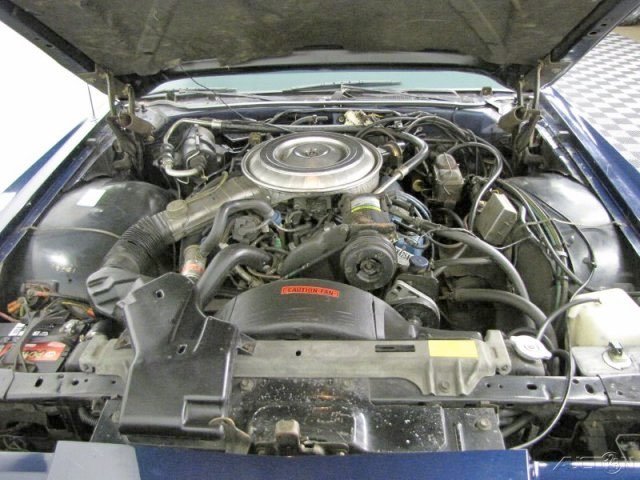 Front view of a car engine with a round air cleaner assembly and various engine components.