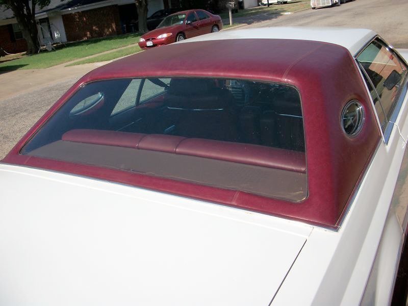 Front windshield and red vinyl roof of a vintage white car parked outdoors.