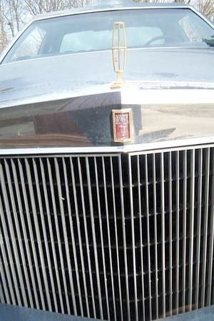 Front view of a vintage car with a large chrome grille and a hood ornament, parked outdoors.