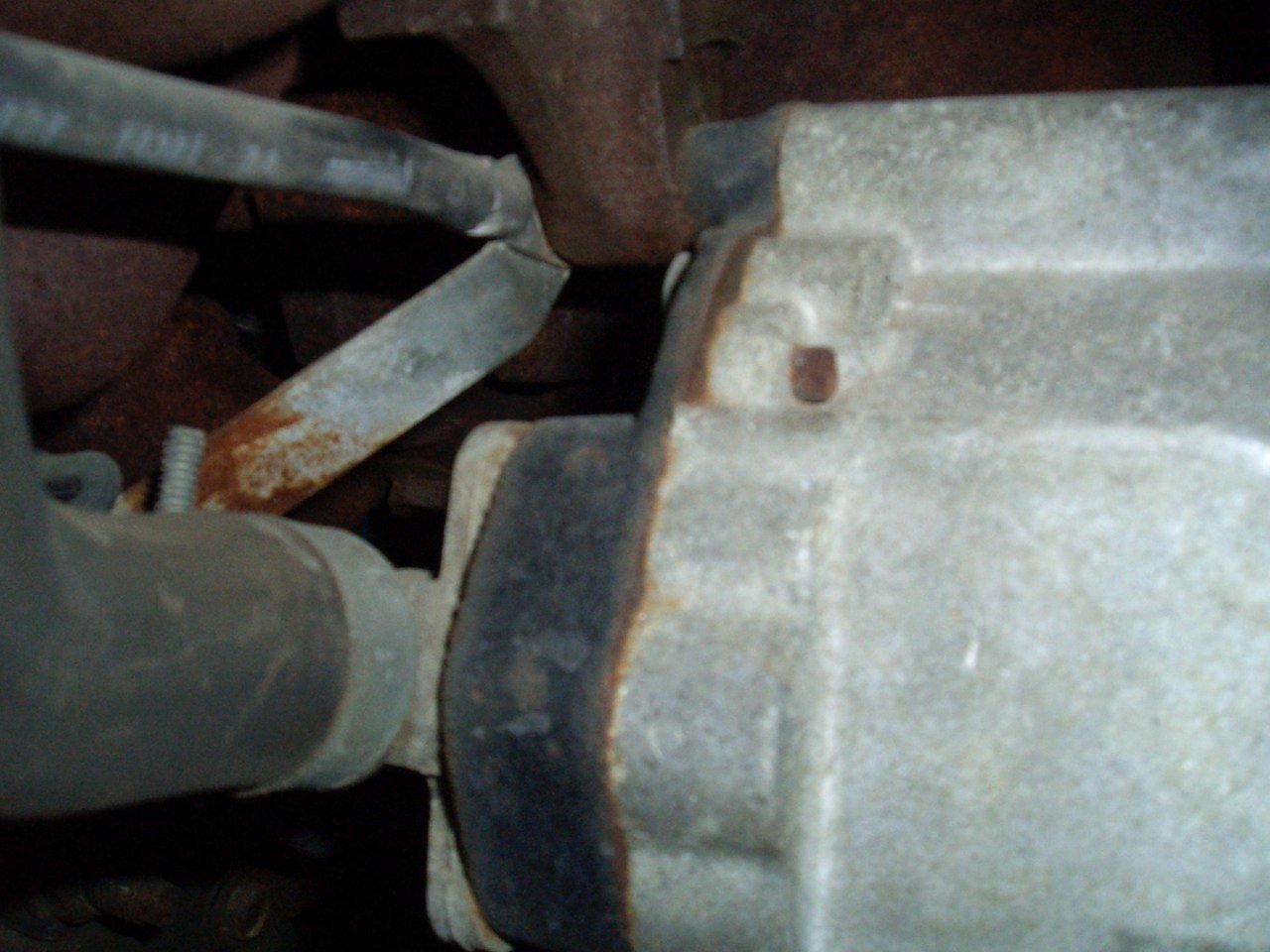 Close-up of a rusty metallic gear shift linkage and transmission housing in a vehicle, showing signs of rust and age.