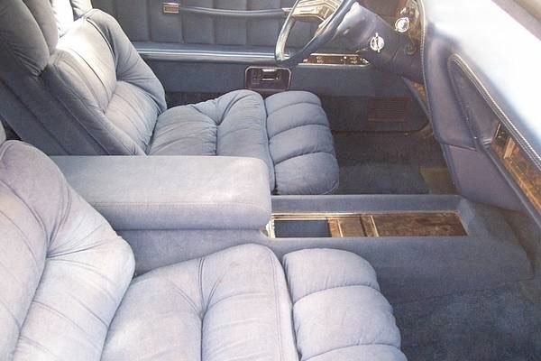Interior of a vintage car showing a plush, blue fabric front seat and section of the dashboard.
