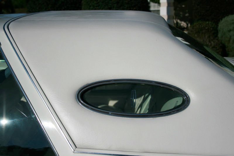 Close-up of the rear white vinyl or leather soft top with a small oval rear window on a vintage or classic car.