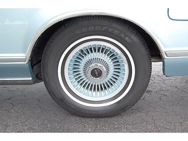 Close-up of a vintage car tire with a whitewall and a distinctive wire-spoke wheel design.