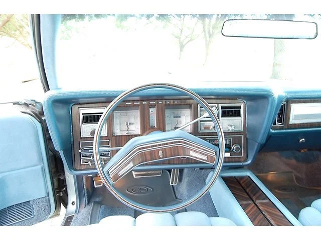 Interior of a vintage car dashboard featuring wood paneling accents, a large steering wheel, and analog gauges.