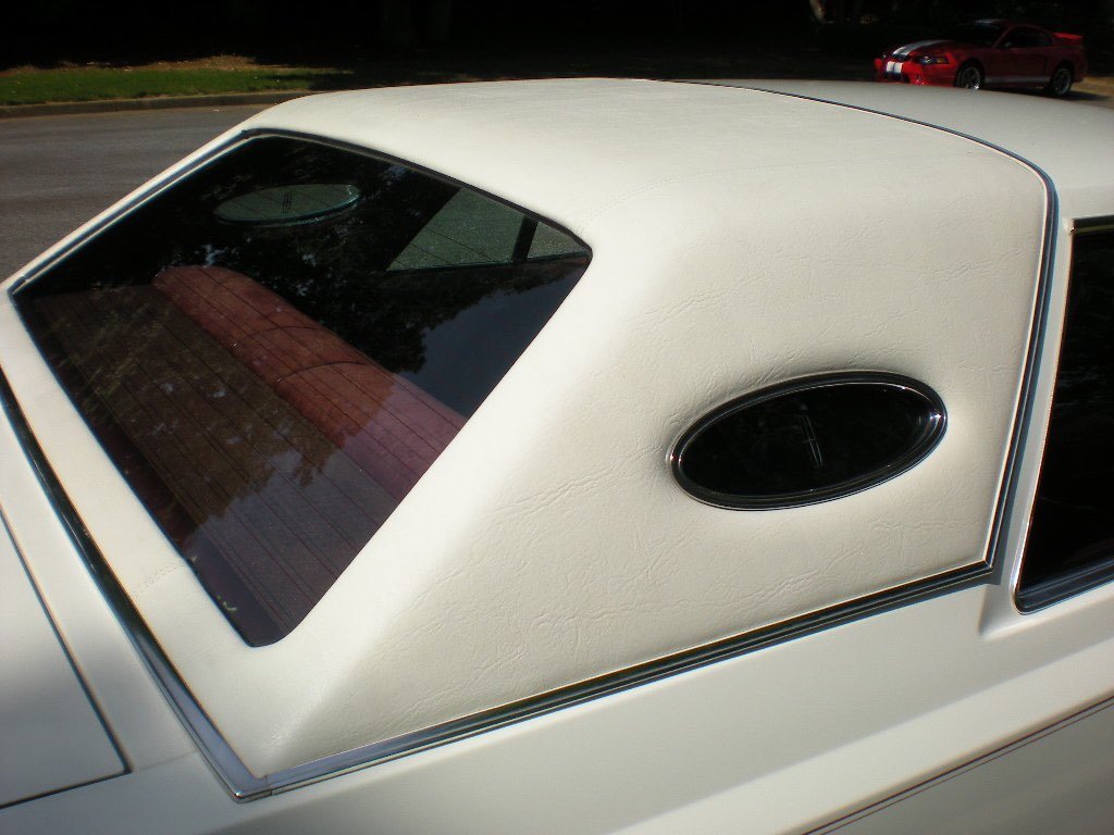 Close-up of a white vintage car with an extra white vinyl roof and a small oval rear window.